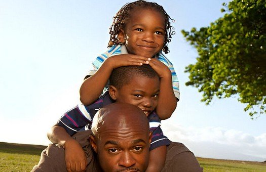 boy sitting on his father's shoulders facing a field in the daytime